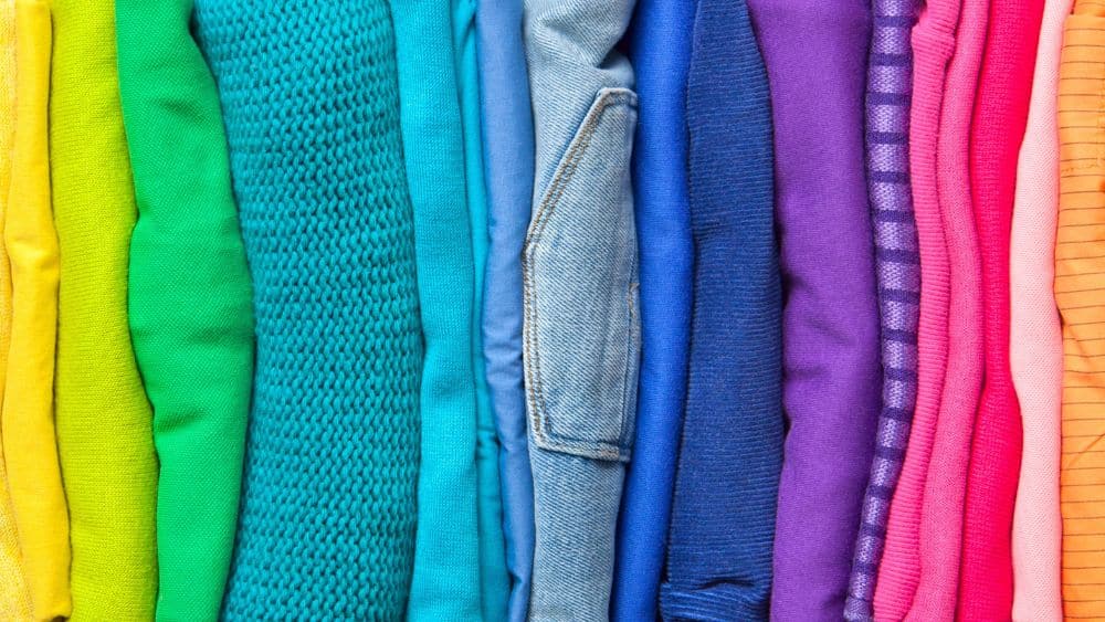 Folded clothes organized by color. The order is yellow, green, blue, purple, pink, and orange.
