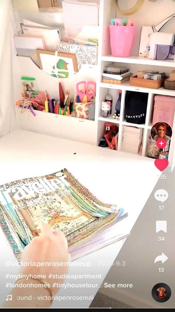 Screenshot of @victoriapenrosemakeup's TikTok video showing a wall-mounted craft shelf that folds down into a table. A hand is reaching for a magazine on the table.