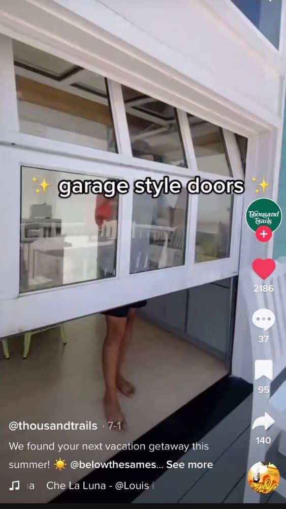 Screenshot of a TikTok from @thousandtrails that shows a white garage door with glass panels rising. Text on the video reads "garage style doors" with sparkle emojis at either end.