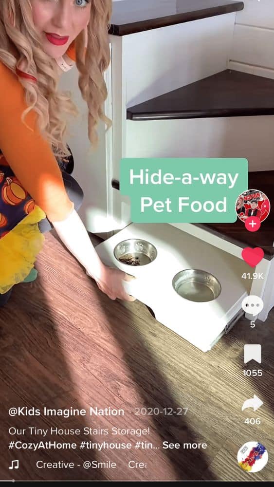 Screenshot of @Kids Imagine Nation's TikTok video showing a person pulling out a pet food and water bowl tray from underneath the bottom step of stairs.